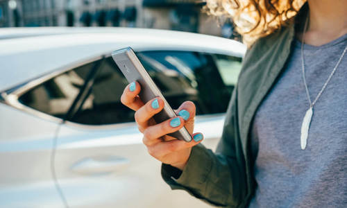 Foto van persoon die een smart phone vasthoudt met auto op de achtergrond